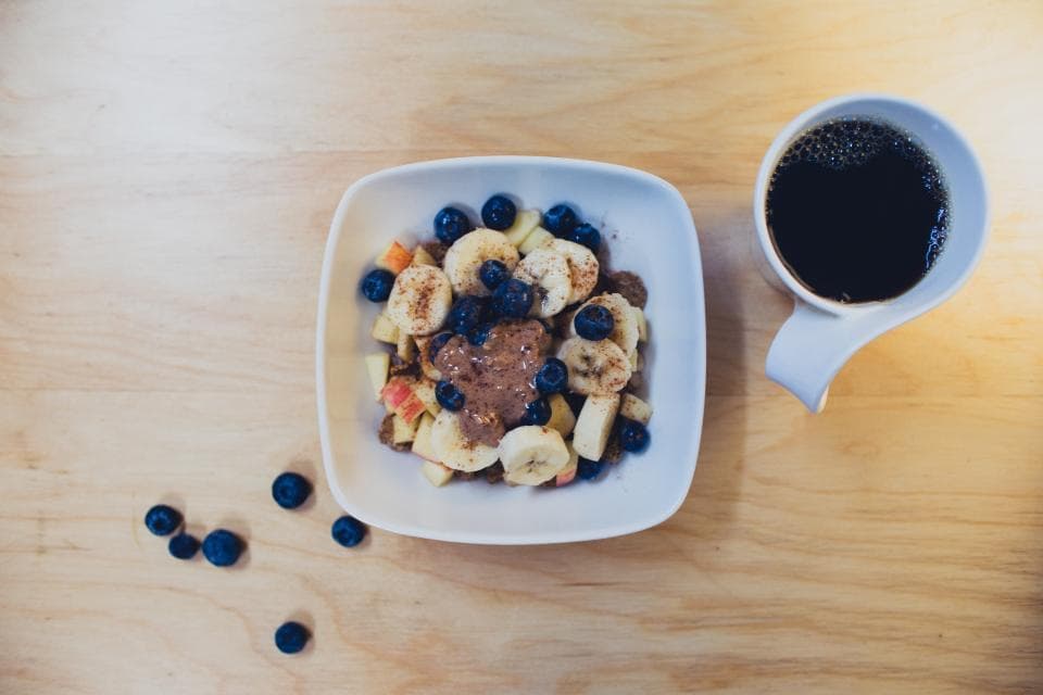 Tazón de avena con plátano y moras junto a una taza de café