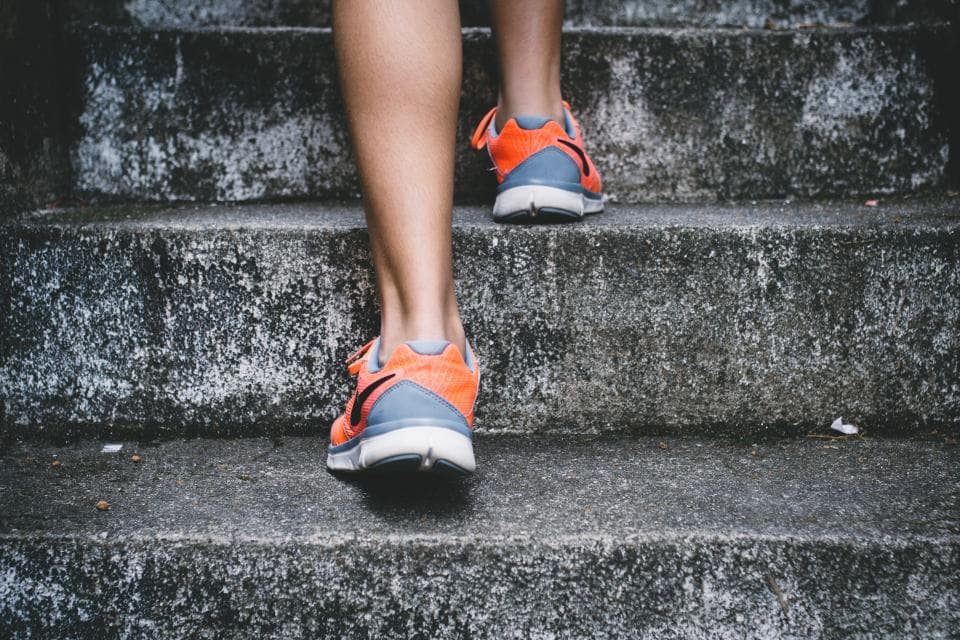 Persona subiendo escalones con tenis naranjas para correr