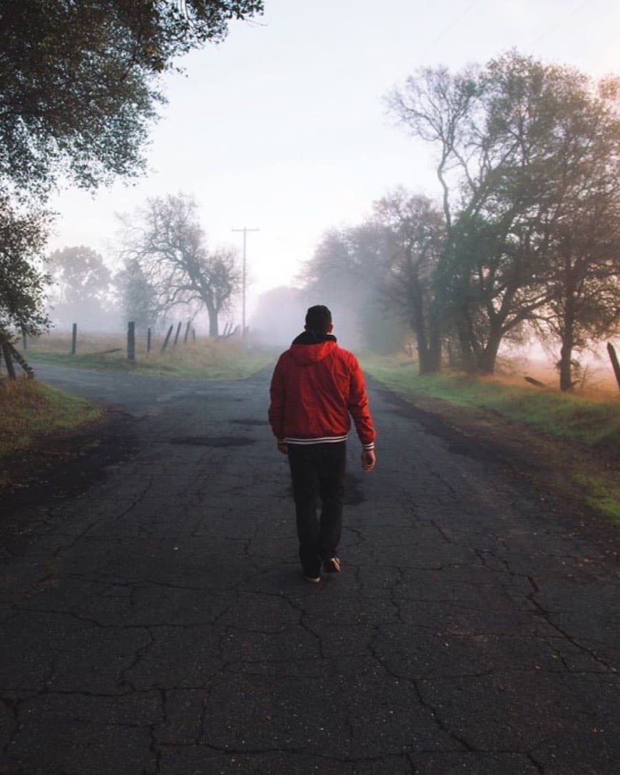 Corredor con chamarra roja en un camino rural con niebla al amanecer